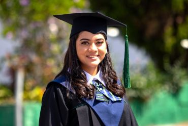 Smiling graduate woman in cap and gown outdoors.