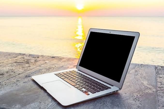 Laptop on stone surface by the sea at sunset.