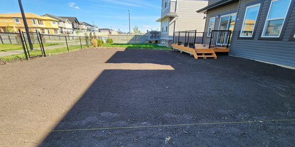 A freshly leveled backyard with dark soil near a house and a small deck.