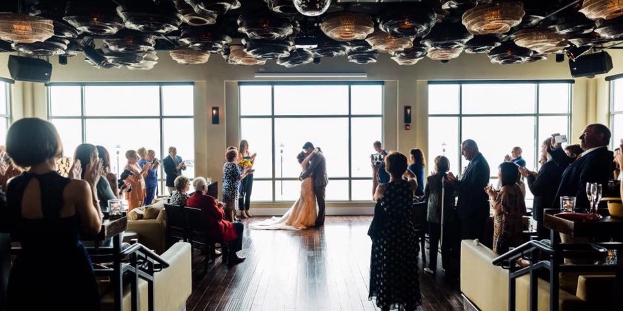 Couple kissing at indoor wedding ceremony with guests applauding.