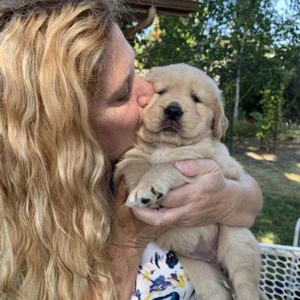 Woman with blonde hair kisses a fluffy golden retriever puppy outdoors.