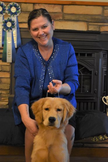 Smiling woman in blue posing with a golden retriever puppy indoors.
