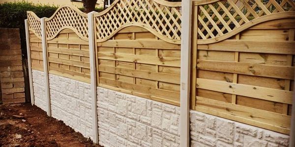 Decorative wooden fence with stone-textured lower panels along a garden path.