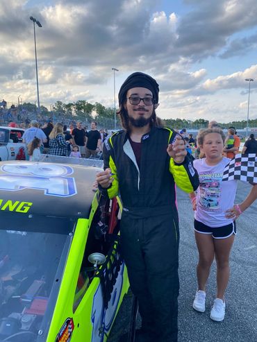 Race car driver celebrating with a girl holding a checkered flag at the track.