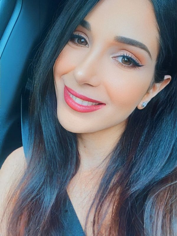 Close-up of a smiling woman with long dark hair and pink lipstick.
