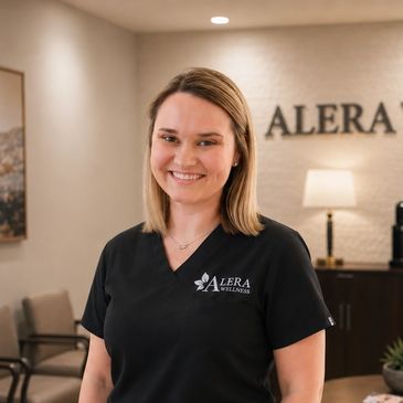 Smiling healthcare professional in Alera Wellness uniform at a welcoming clinic reception area.