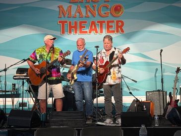 Three men playing guitars on stage at Little Mango Theater.