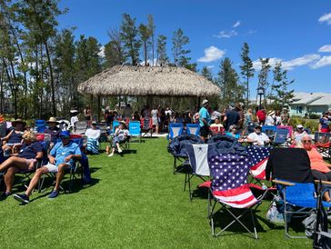 People relaxing on chairs outdoors near a thatched-roof pavilion under a clear blue sky.