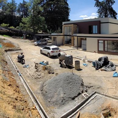 Modern house under construction with building materials and vehicles outside.