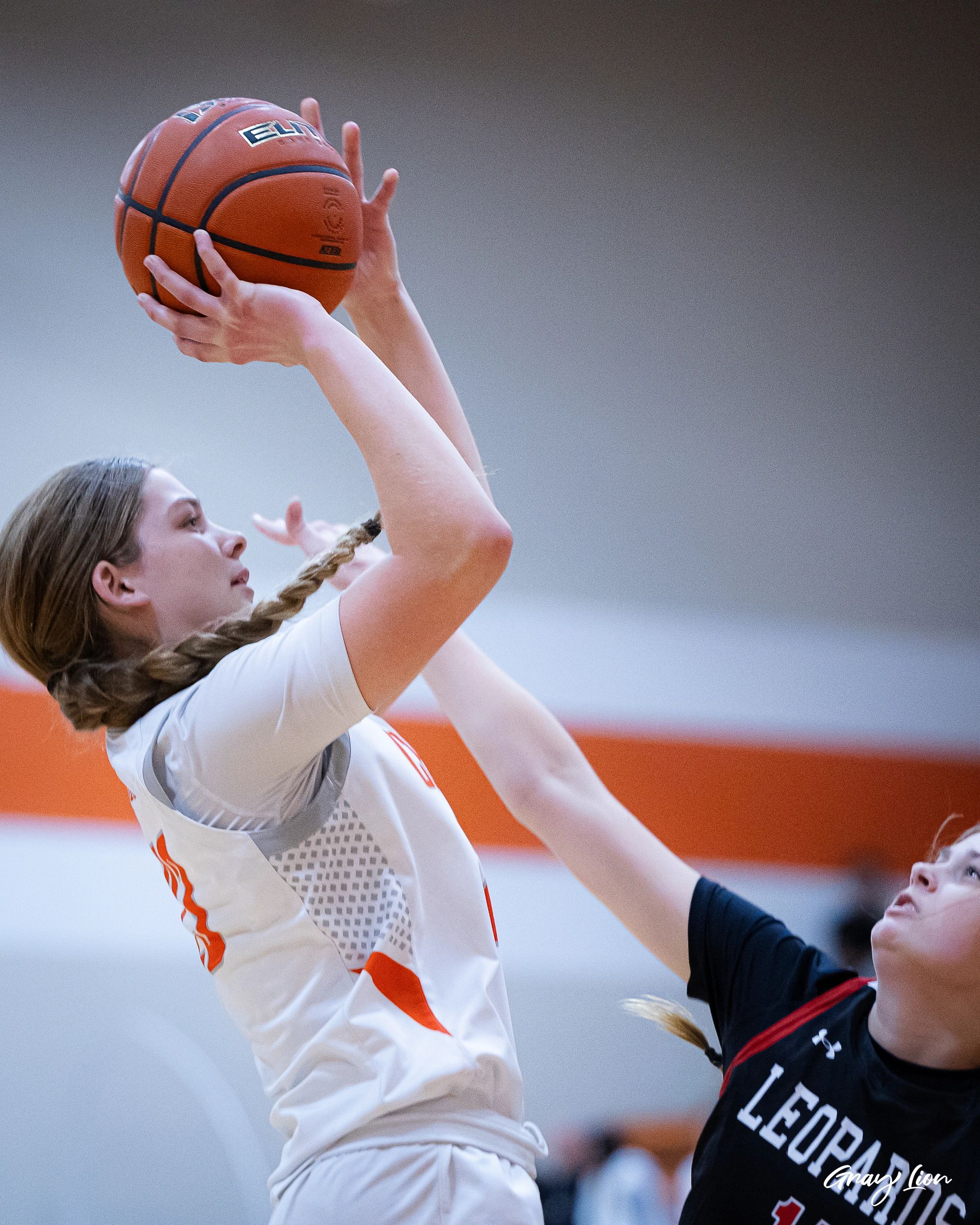 Female basketball player shooting with defender blocking.