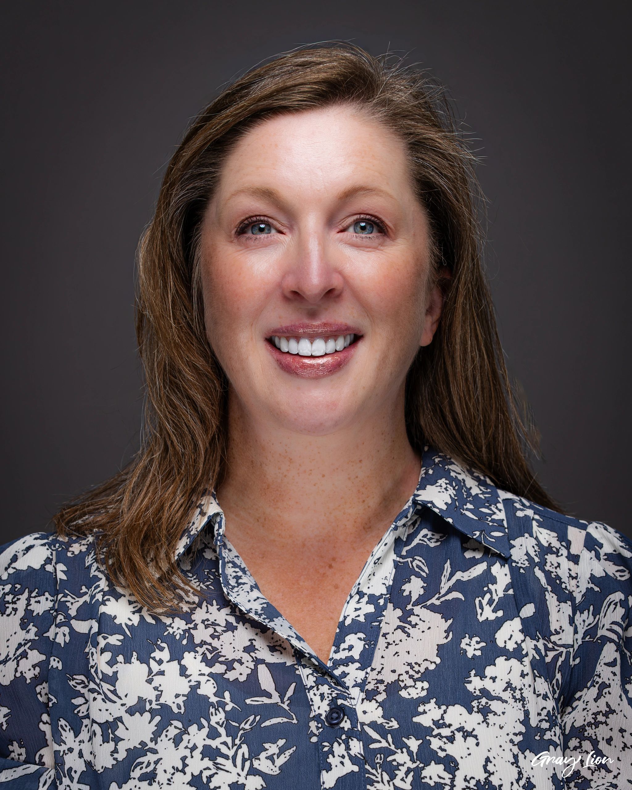 Close-up of a smiling woman with blue eyes and a patterned shirt.