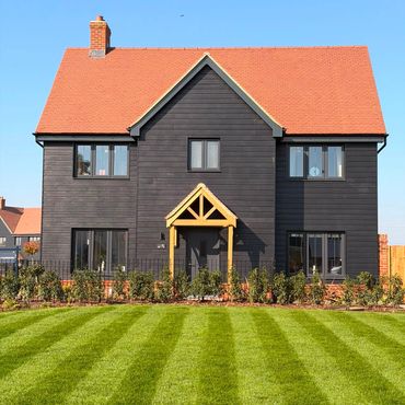 Modern black wooden house with a red roof and striped lawn.