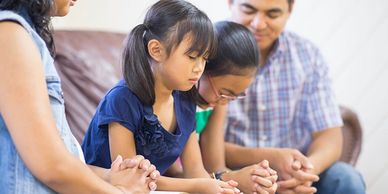 Family sitting together, praying with closed eyes and holding hands.