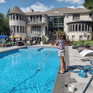 A person cleaning a large pool in front of a luxurious house on a sunny day in vaughan ontario
