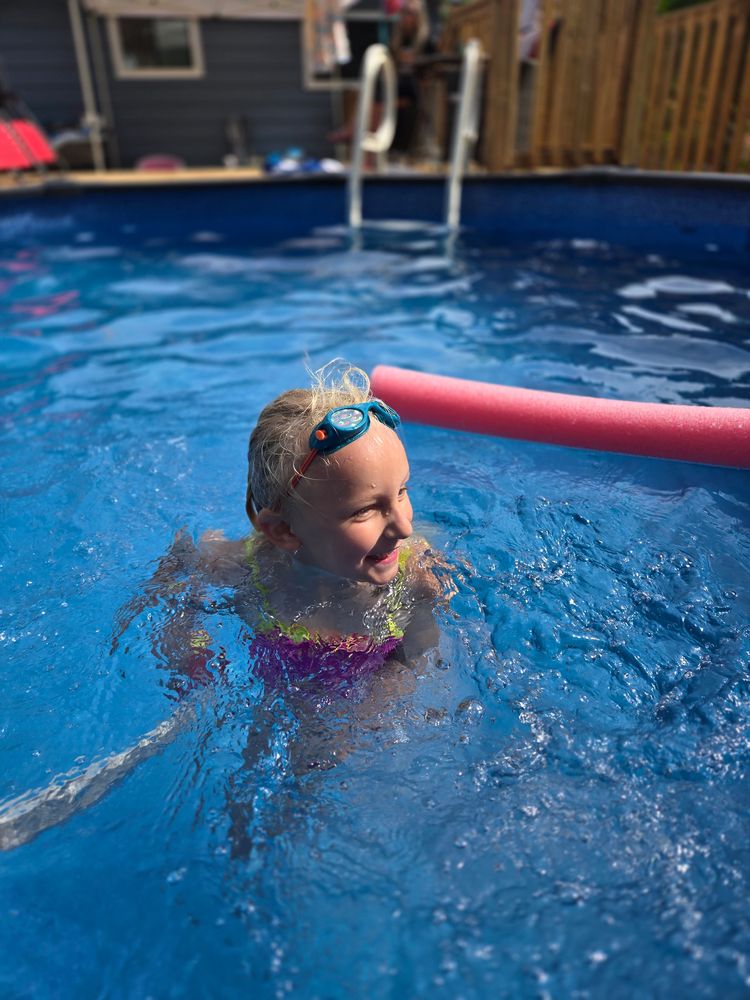 A joyful child swimming in a pool with goggles and a pink pool noodle. simcoe county