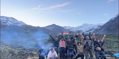 Group of people joyfully jumping in front of mountains with a campfire.