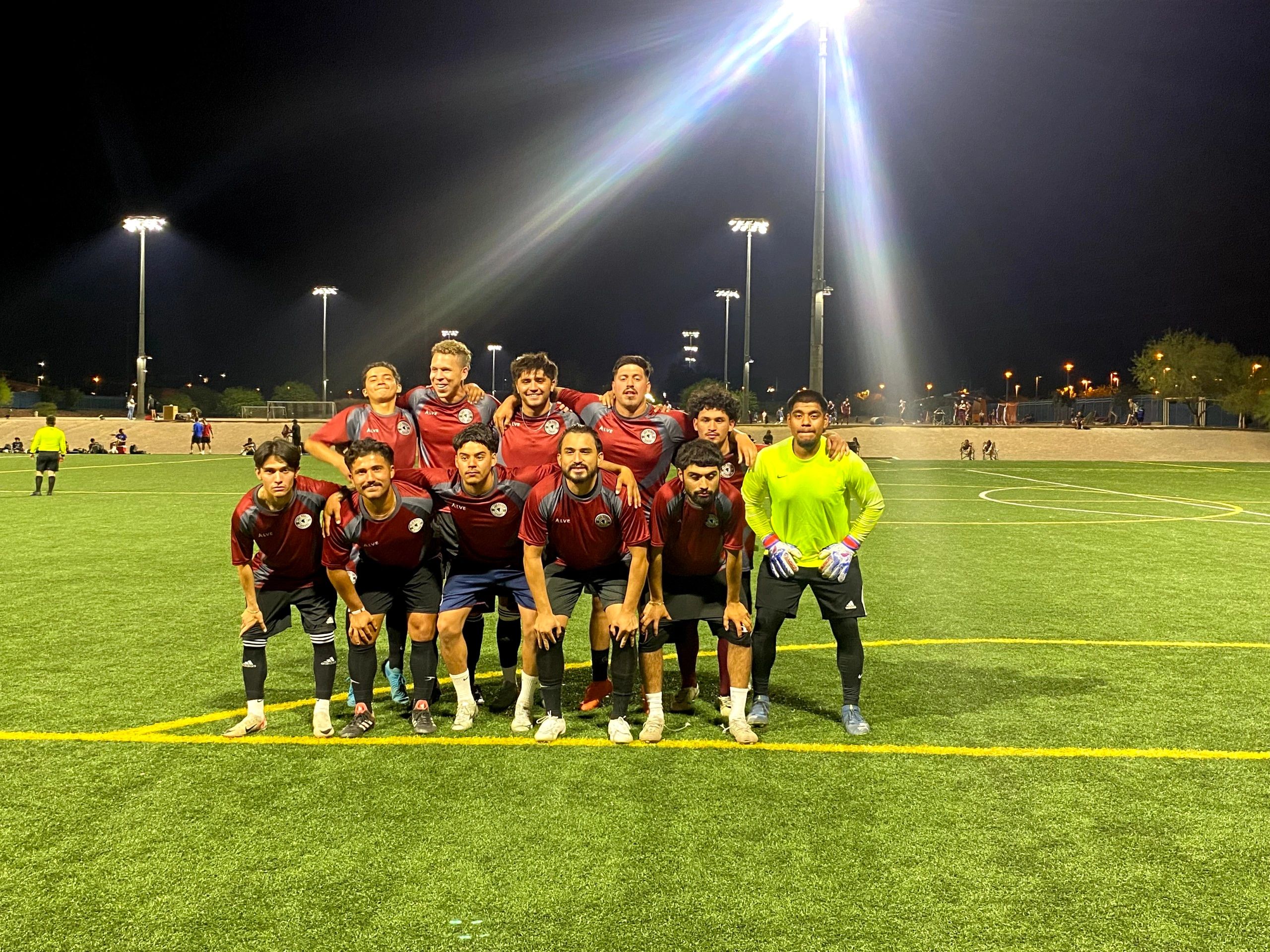 A soccer team posing on a field at night under bright lights.
