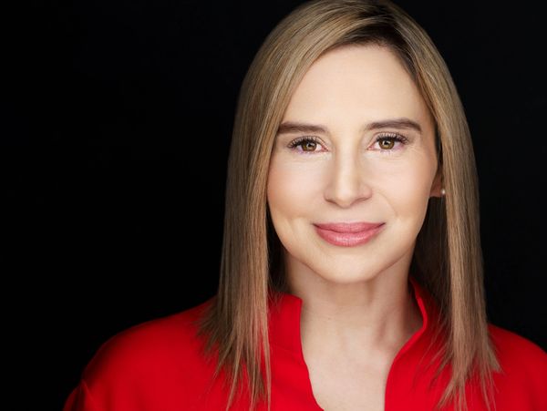 Confident woman with straight blonde hair wearing a red top against a black background.
