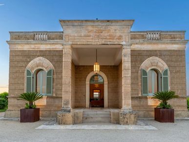 Historic stone building with arched windows and central entrance under clear blue sky.