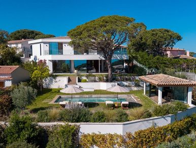 Modern white villa with a pool and outdoor seating under a clear blue sky.