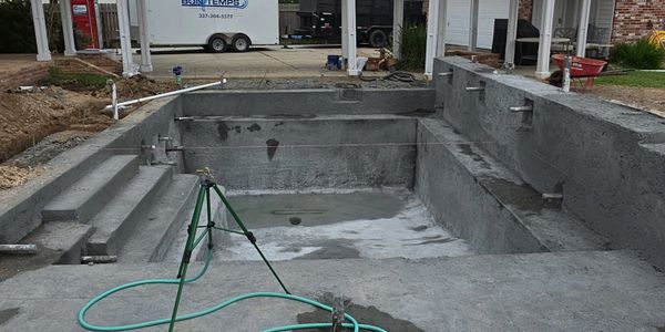 An unfinished concrete swimming pool under construction in a backyard.
