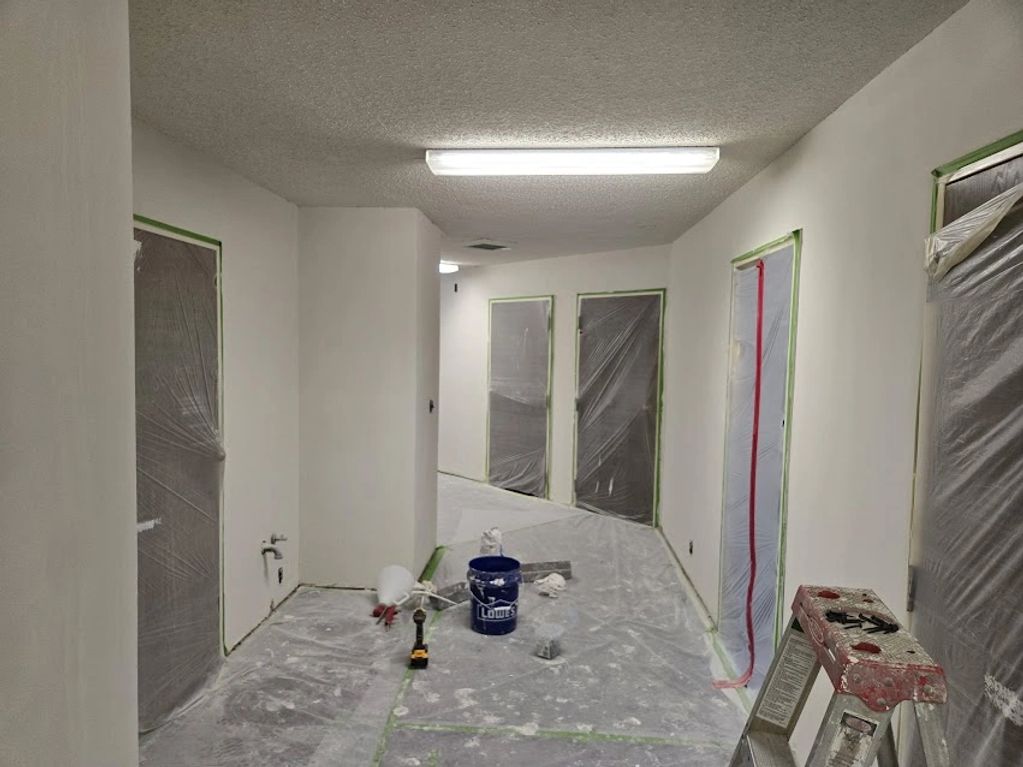 Hallway under renovation with covered doors and painting supplies.