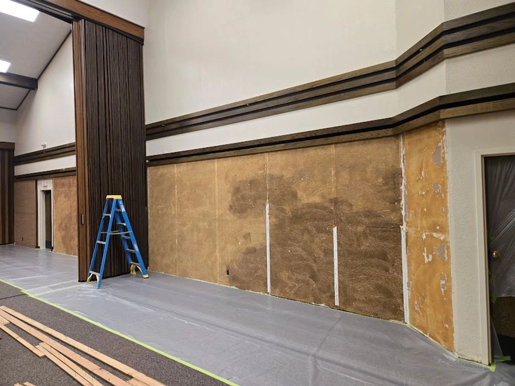 Interior wall renovation with a ladder and protective floor covering.