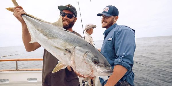 Two men on a boat proudly hold a large fish they caught at sea.