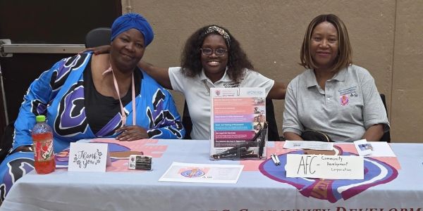 Three women sitting behind a community development table.
