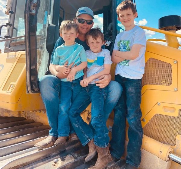 A man with three boys sitting on a yellow construction vehicle under a blue sky.