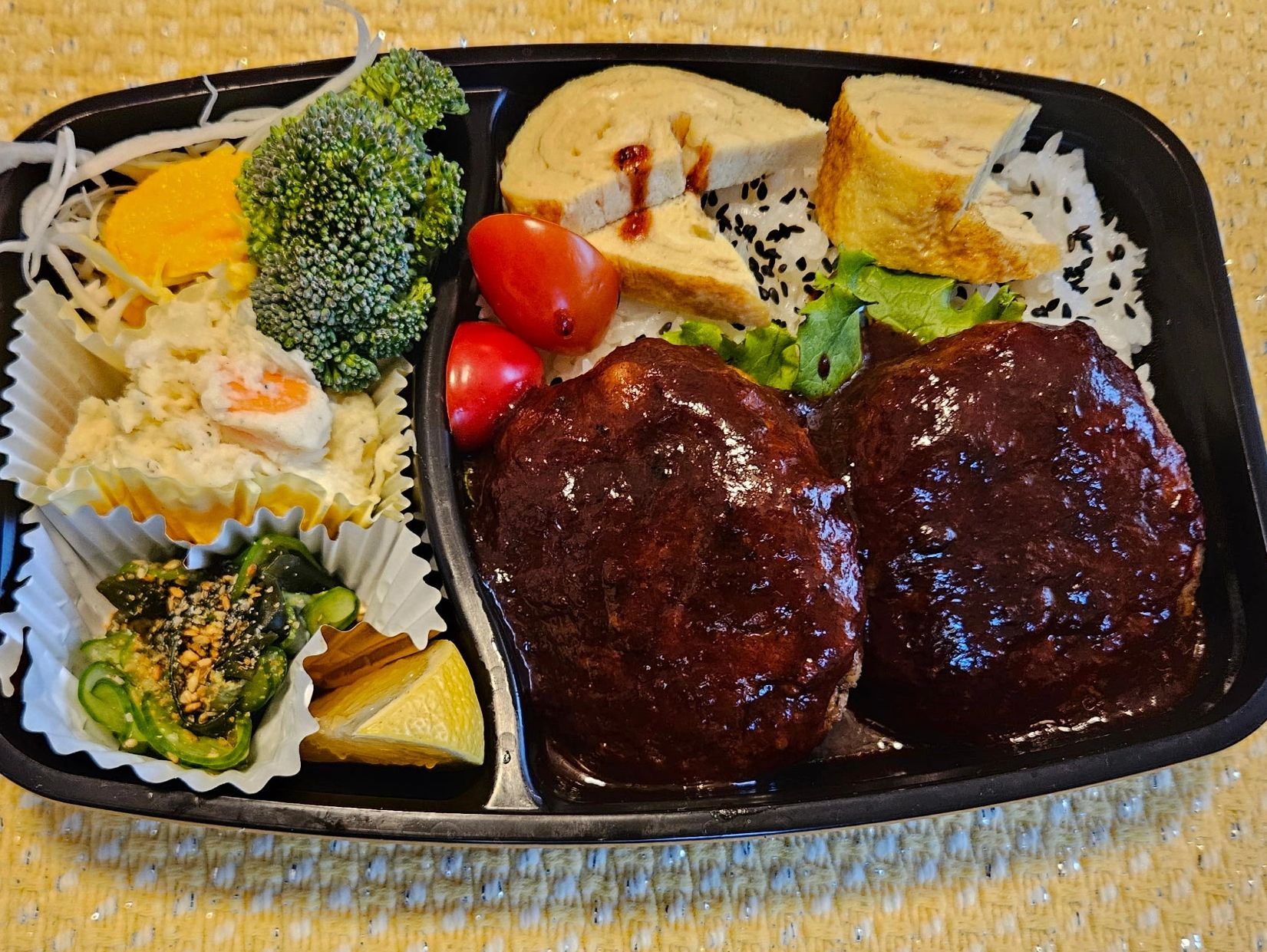 Japanese bento box with hamburger steaks, rice, tamagoyaki, and vegetables.
