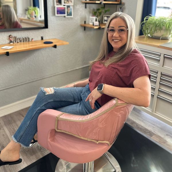 Smiling woman with glasses sitting comfortably in a pink chair.