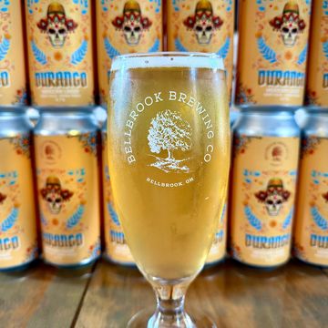 A glass of Bellbrook Brewing Co. beer with colorful Durango cans in the background.