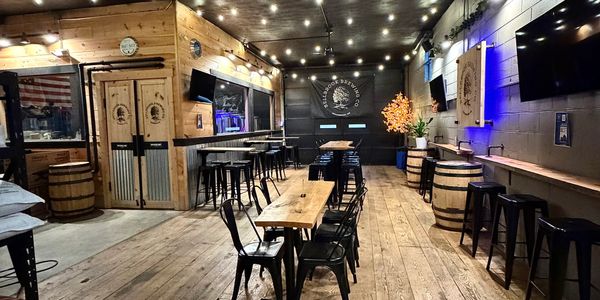 Cozy rustic bar with wooden floors, barrels, and string lights.