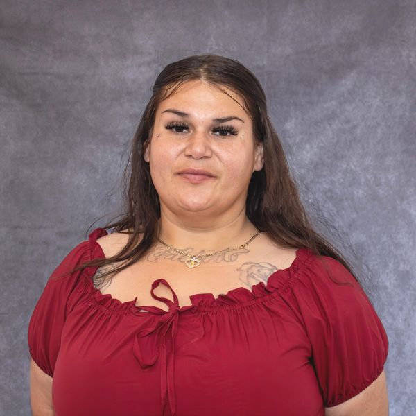 Woman with long dark hair wearing a red blouse against a gray backdrop.