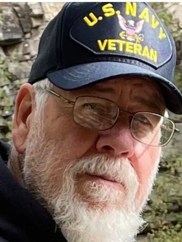 Older man wearing a U.S. Navy veteran cap and glasses.
