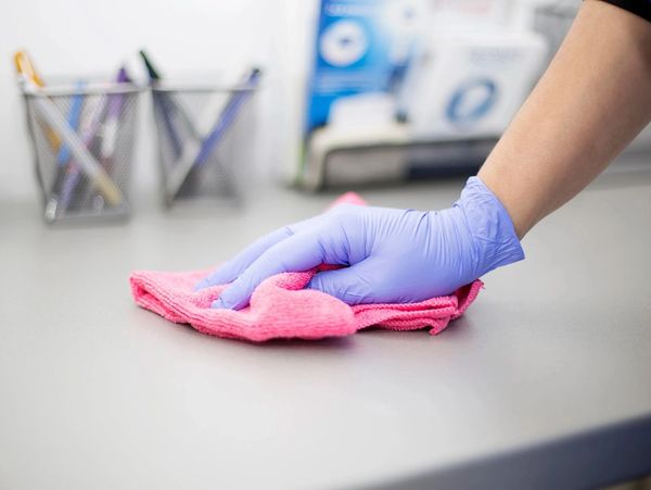 Worker with blue gloves cleaning a desk with a pink cloth