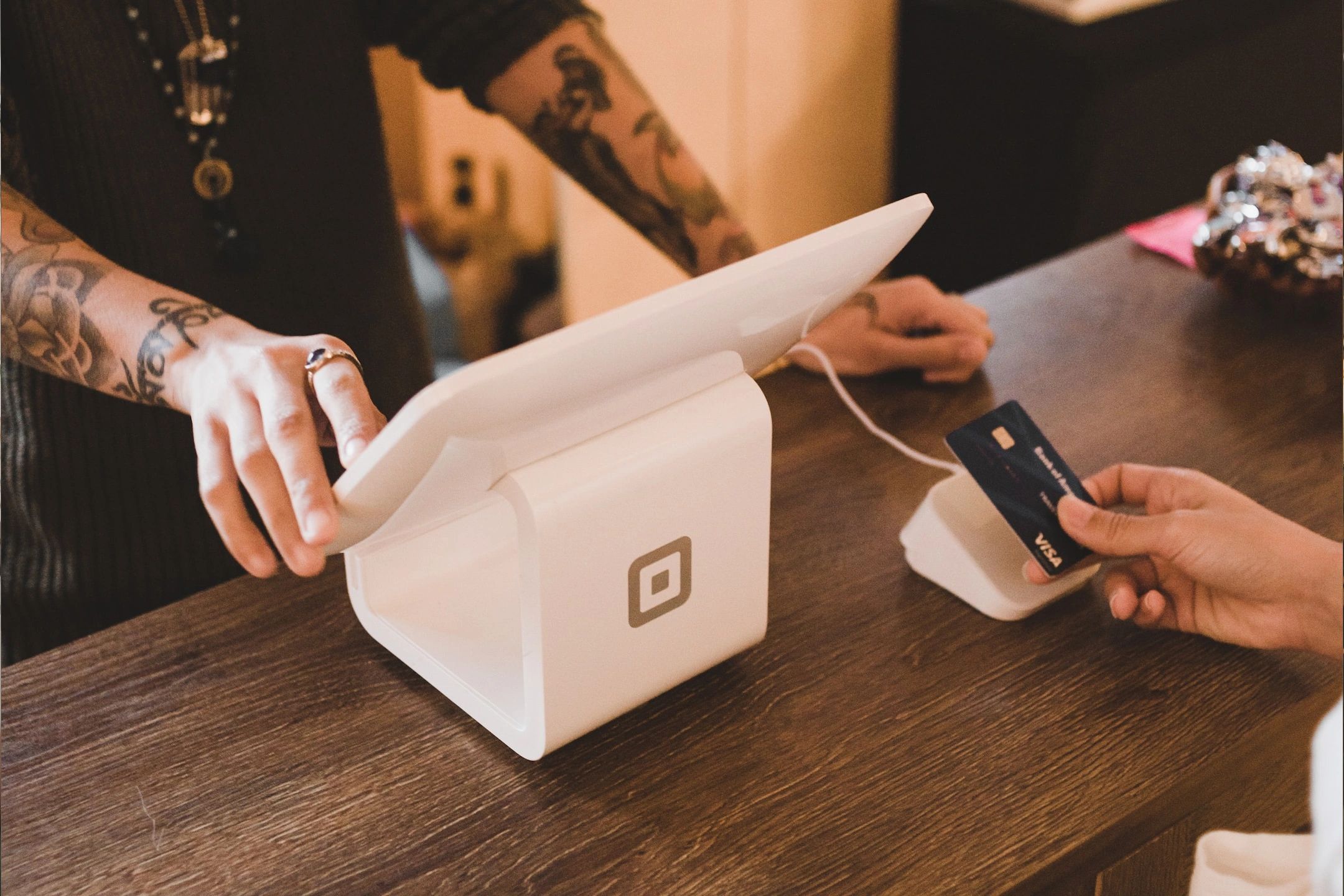Person with tattoos on arms collecting payment from someone else through a credit card POS.