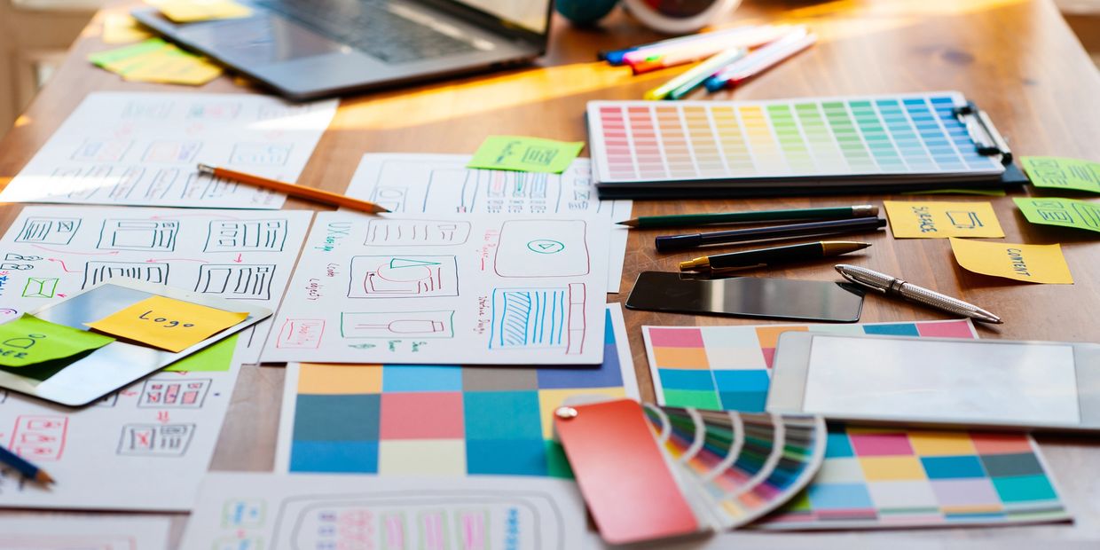 Desk covered in color swatches, sketches, and rebranding materials.