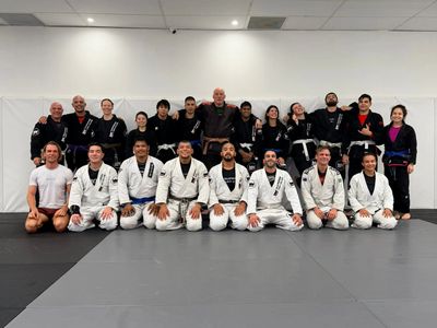 Group photo of Brazilian Jiu-Jitsu practitioners in gis and belts at a martial arts gym.