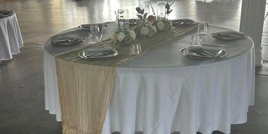 Elegant round table set with white linens and gold runner for a formal event.