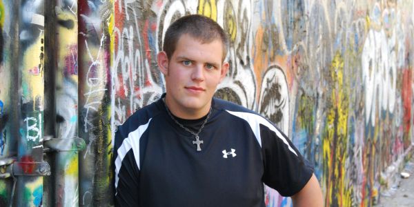 Young man leaning against a graffiti-covered wall.