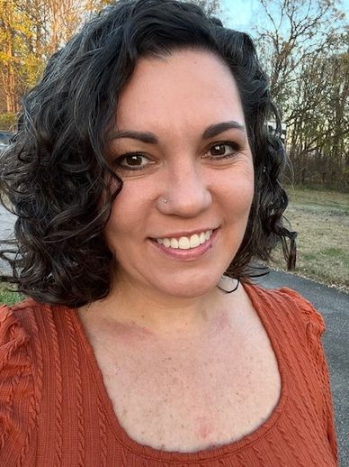 Woman with curly hair smiling outdoors in an orange top.