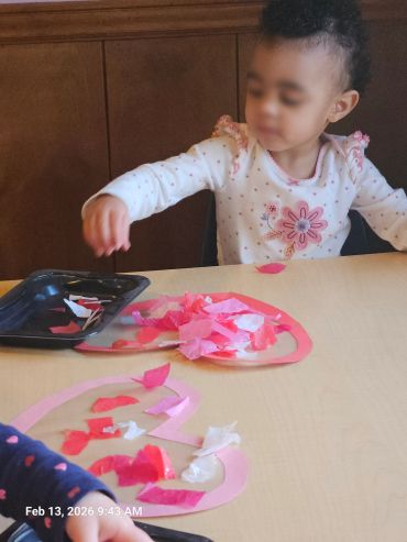 A child creating a Valentine-themed craft with pink and red paper pieces.