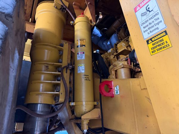Close-up of yellow heavy machinery with warning labels and hydraulic components.