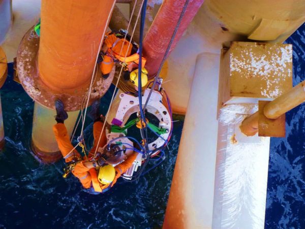 Workers in safety gear performing maintenance on an offshore oil rig.