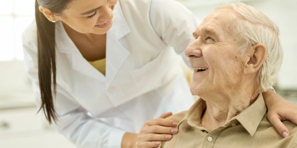 A caregiver smiling warmly at an elderly man, showing support and care.