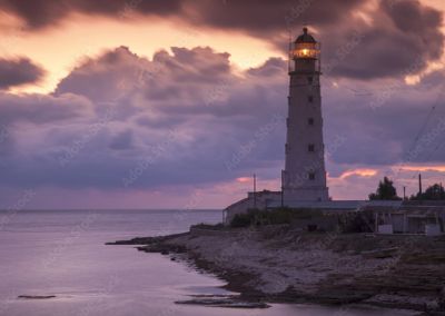 Lighthouse illuminated at sunset by the sea.
