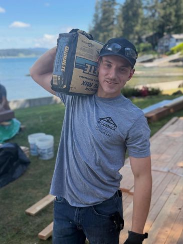 Young man carrying a bag of concrete mix on his shoulder outdoors.