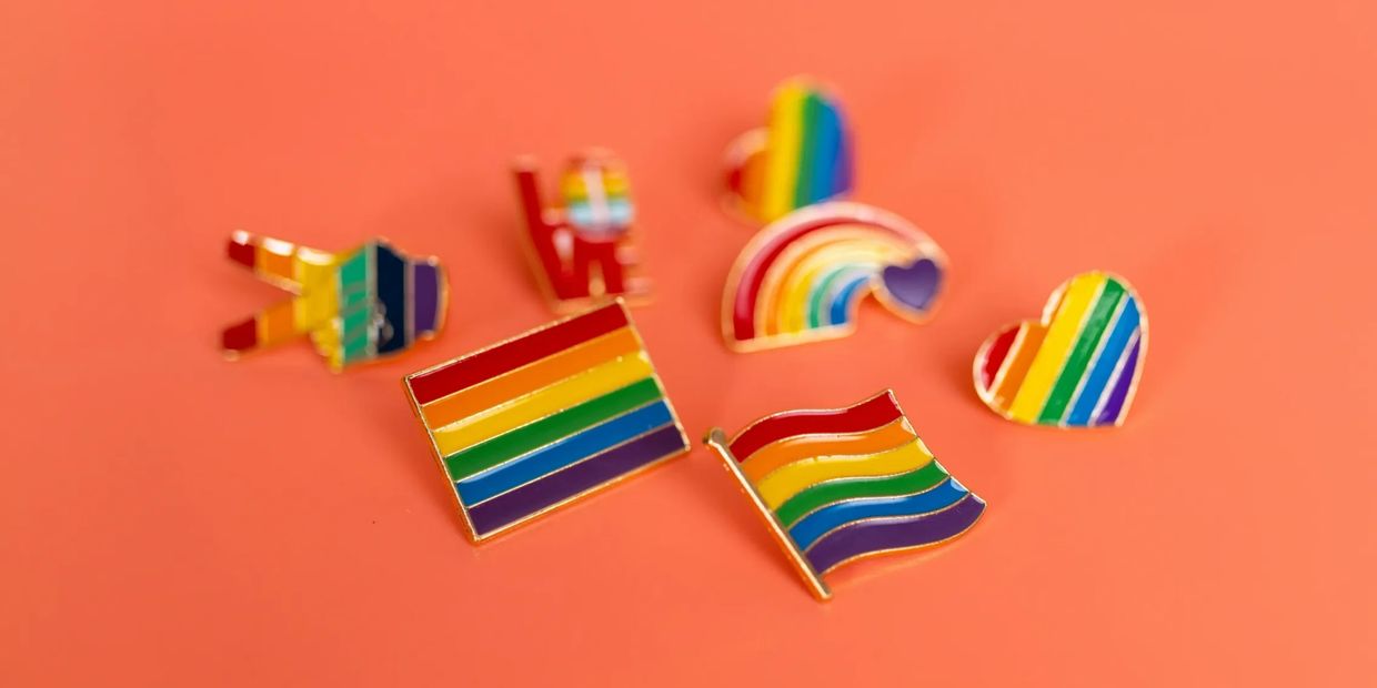 Colorful LGBTQ+ pride pins on an orange background.